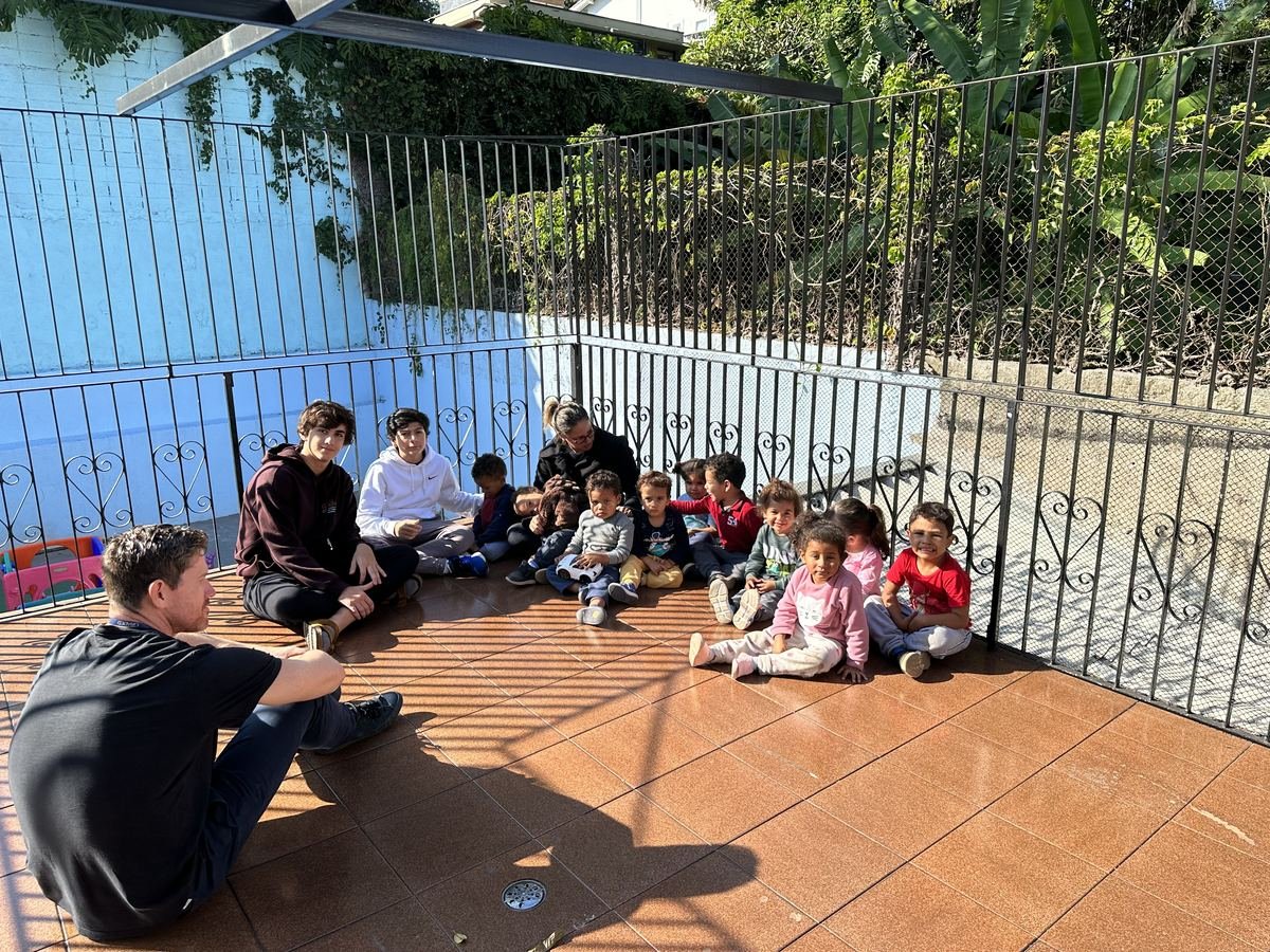 Founders and a teacher sitting with daycare children on a sunny terrace