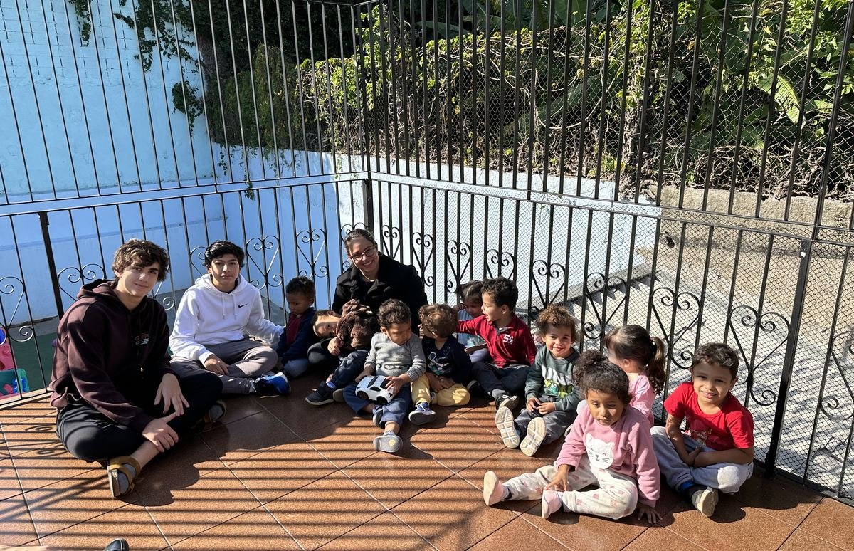 The two founders sitting on a terrace with a group of daycare children during the first visit in 2023