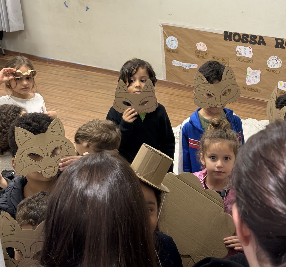 Two Rise Up Co members, seen from behind, greeting children wearing cardboard animal masks