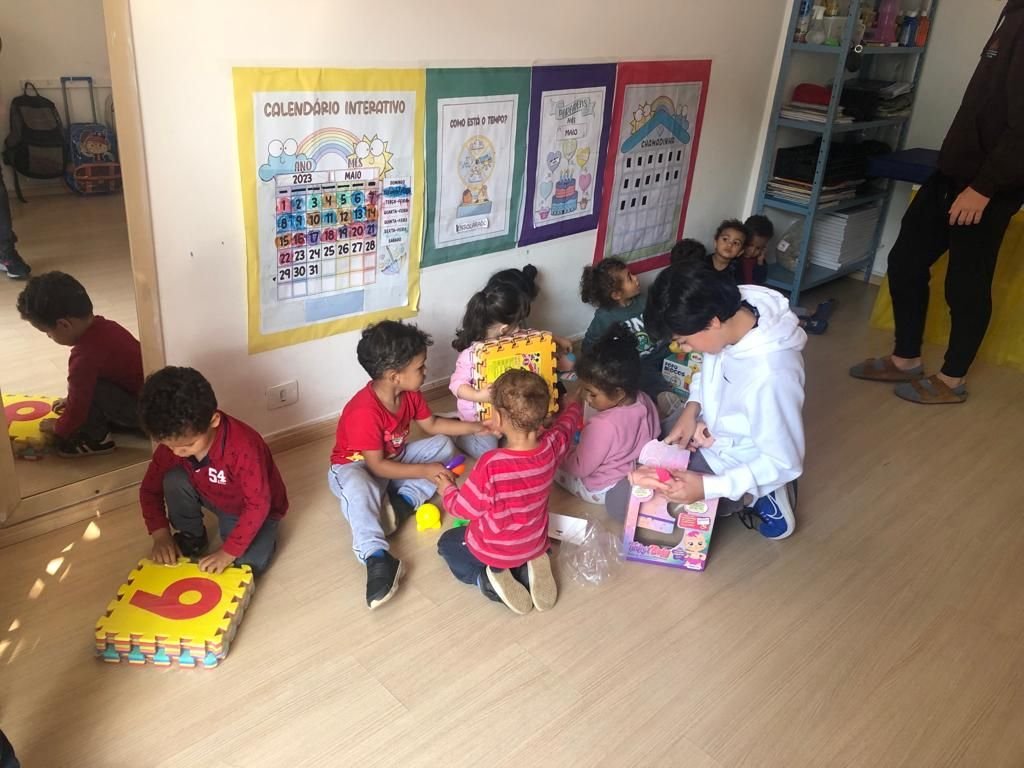 A Rise Up Co member sitting on the daycare floor with a group of toddlers as they open new toys